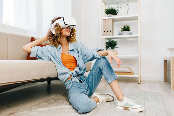 Улыбающаяся женщина наслаждается игрой виртуальной реальности дома с футуристическими очками виртуальной реальности на диване в современной гостиной - Фото, изображение