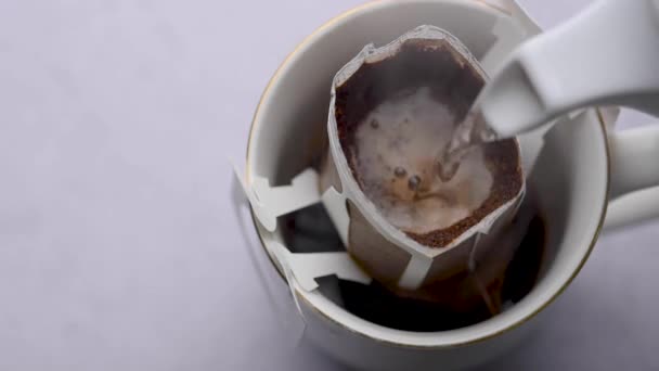 Heißes Wasser wurde in eine Tasse gerösteten Kaffees gegossen, um frischen Tropfkaffee zu produzieren. Kaffeezubereitung mit Tropfkaffeesack - Filmmaterial, Video