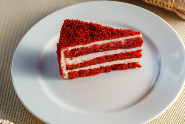 Stuk van rode fluwelen taart rust op een ongerepte witte plaat, nodigen u uit om zijn rijke smaken te proeven met elke hap. - Foto, afbeelding