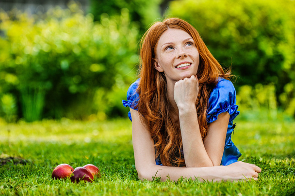 червоноволоса усміхнена молода жінка лежить на траві
 - Фото, зображення
