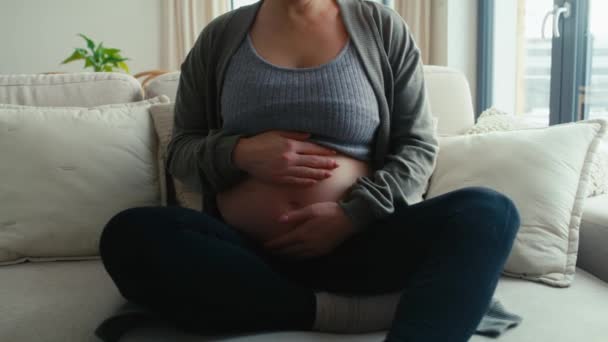 Felismerhetetlen kaukázusi terhes nő ül a kanapén, és megérinti a has - Felvétel, videó