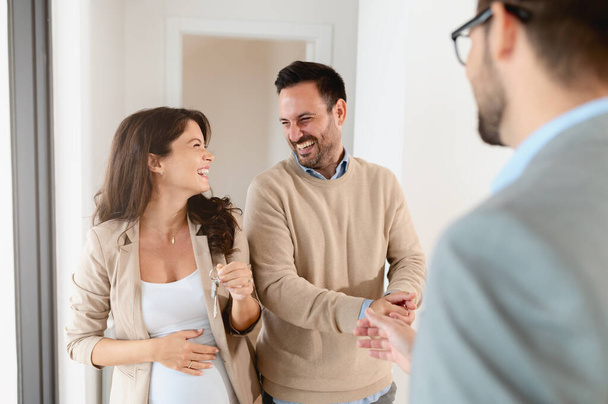 Мужчина и его беременная жена, разговаривают с агентом по недвижимости, посещающим квартиру для продажи или аренды. Будущие родители покупают квартиру. Концепция недвижимости - Фото, изображение