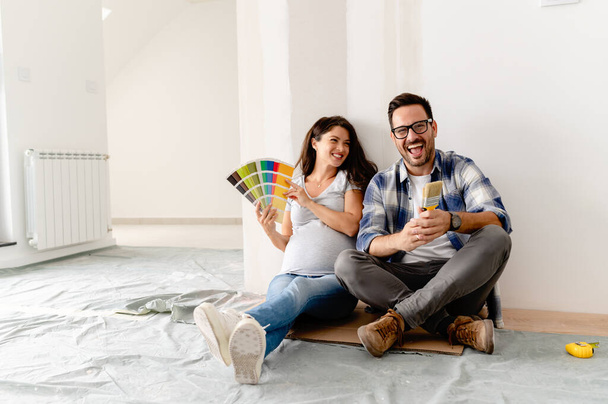вагітна жінка і її чоловік вибирають колір фарби для фарбування стін в новій квартирі - Фото, зображення
