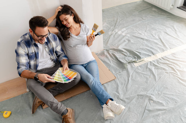 妊娠中の女性と彼女の夫は新しいアパートで壁を塗るための絵の色を選択します - 写真・画像