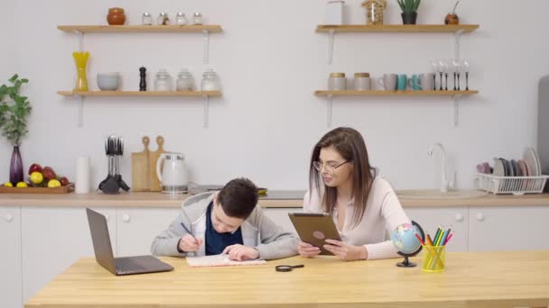 Äiti ja aikuinen poika opettavat kotitehtäviä kotona, äiti auttaa poikaa tekemään kotitehtäviä - Materiaali, video