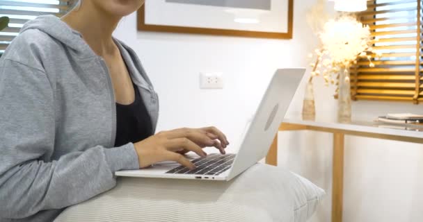 Boldog ázsiai nő használja fejhallgató zenét hallgatni online web konferencia ül a kényelmes kanapén nappaliban otthon. Az otthoni kutatásban dolgozó ázsiai nők online e-learning videohívást néznek - Felvétel, videó