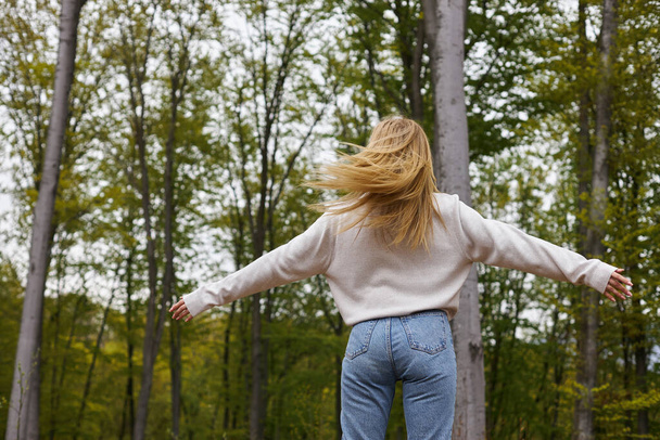 Вид ззаду блондинка-дослідник танцює в лісі в мальовничій мирній обстановці, свобода - Фото, зображення