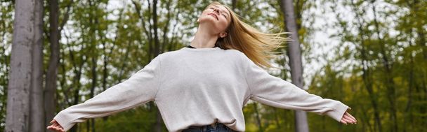 Peaceful and relaxed blonde woman dancing in forest jeans and sweater on backpacking trip, banner - Foto, immagini