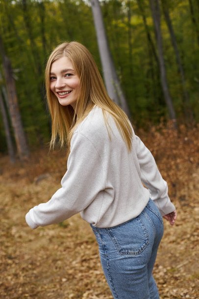 Radosna młoda kobieta spacerowiczka biegnąca w jesiennych lasach i patrząca w kamerę z uśmiechem - Zdjęcie, obraz
