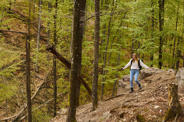 Junge blonde Frau trägt Rucksack beim Wandern und zu Fuß auf felsigen Klippen mit Daunen - Foto, Bild