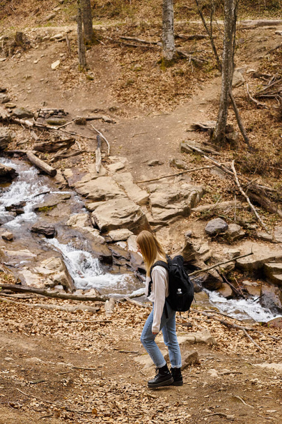 Young blond trekker with travel backpack, walking near forest stream enjoying views - Photo, Image
