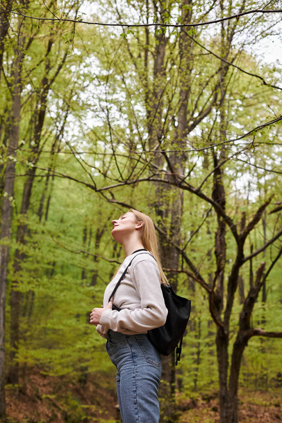 Zijaanzicht van gezellige ontspannen blonde vrouw wandelaar rusten met gesloten ogen in het bos uitzicht - Foto, afbeelding