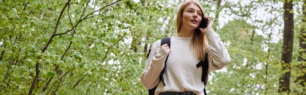 Zdjęcie blondynki ładna kobieta podróżnik z plecakiem mówi przez telefon chodzenie po ścieżce leśnej, sztandar - Zdjęcie, obraz
