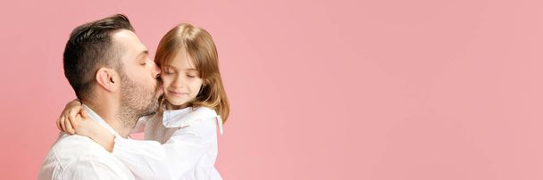 Banner. Pai beijando sua adorável filhinha contra fundo pastel rosa com espaço negativo para inserir texto. Conceito de Dia Internacional da Felicidade, infância e paternidade, positivo. Anúncio - Foto, Imagem