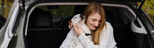 Obraz kobiety delikatnie przytulającej swojego białego psa siedzącego z tyłu samochodu, psi sztandar - Zdjęcie, obraz