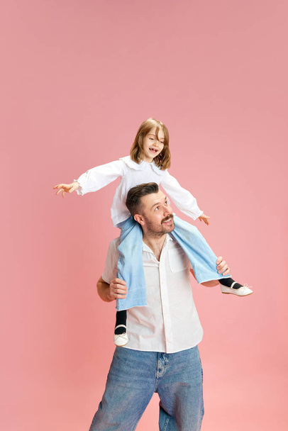 Pai alegre carregando filha em seus ombros. Criança e pai se divertindo juntos. contra fundo pastel rosa. Conceito de Dia Internacional da Felicidade, Dia dos Pais, positivo. Anúncio - Foto, Imagem