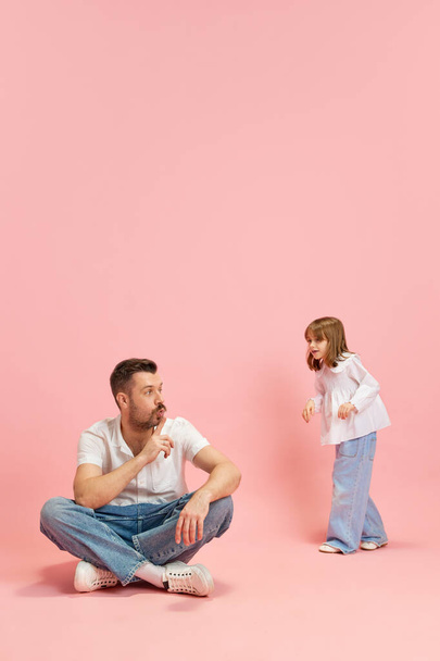 Сидячий чоловік, тато жестикулює, щоб мовчати, щоб ходити так голосно і говорити дитину на рожевому пастельному тлі. Концепція Міжнародного дня щастя, дитинства та батьківства, емоцій. Реклама - Фото, зображення