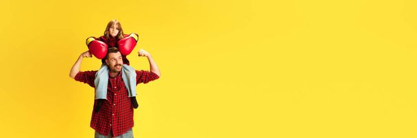 Pankart. Boks eldivenleriyle babalarının omuzlarında oturan küçük bir çocuk ve parlak sarı arka planda negatif alana karşı somurtuyor. Uluslararası Mutluluk Günü kavramı, Babalar Günü. Ad - Fotoğraf, Görsel