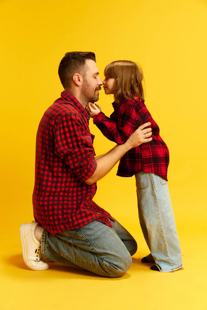 Apa és én. Térdelő apa és gyermek összeillő ruhák érintik orr ellen élénk sárga háttér. A boldogság, gyermekkor és szülőség nemzetközi napjának koncepciója, Apák napja. Hirdetés - Fotó, kép