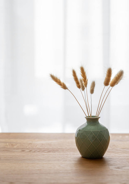 Tischplatte aus Eiche aus Holz mit einer grünen Vase mit trockenen Blumen und mit freiem Platz für die Installation eines Produkts oder Layouts vor einem Fensterhintergrund. Freiraum für Text. - Foto, Bild