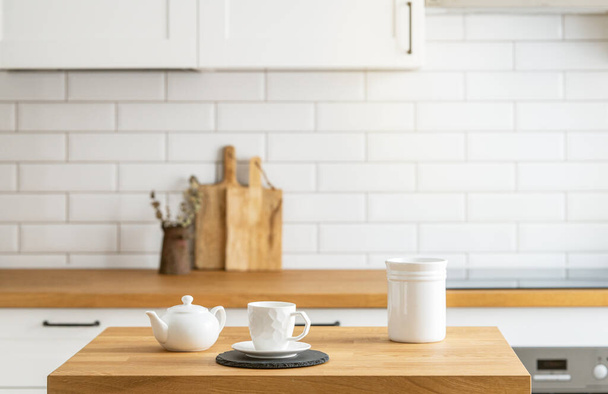 白いレンガの背景を持つキッチンの前に紅茶とケトルが付いている木製のオークテーブル. スカンジナビアスタイルの居心地の良い朝食コンセプト.  - 写真・画像