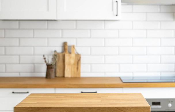 Holztisch aus Eichenholz mit freiem Platz, um ein Produkt oder Lebensmittel vor einer unscharfen weißen Küche mit Backsteinhintergrund anzuzeigen oder zu bewerben. Das Konzept eines gemütlichen Hauses im skandinavischen Stil. - Foto, Bild