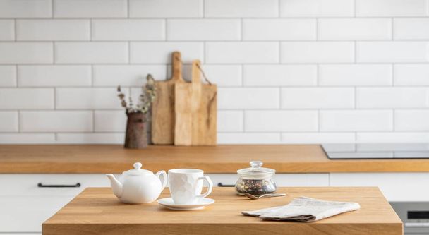 白いレンガの背景を持つキッチンの前に紅茶とケトルが付いている木製のオークテーブル. スカンジナビアスタイルの居心地の良い朝食コンセプト.  - 写真・画像