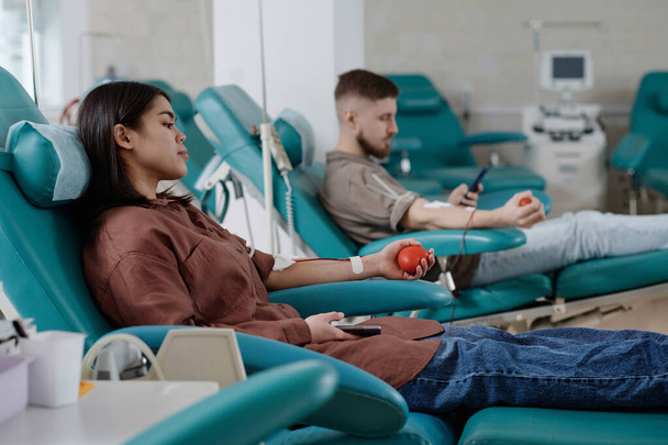 Mężczyźni i kobiety dawcy krwi siedzący w fotelach kliniki podczas procesu transfuzji, skupić się na kobiecie - Zdjęcie, obraz