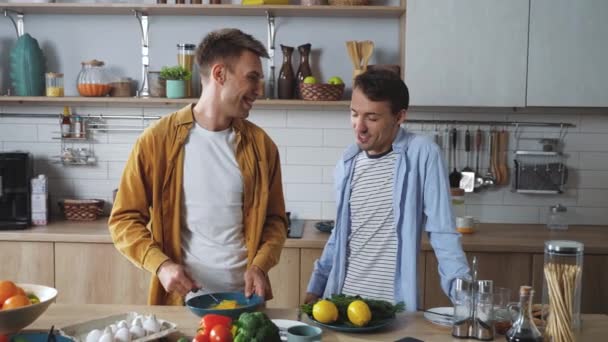 Una alegre pareja gay masculina preparando el desayuno juntos en la cocina. Feliz atractivo joven adulto hombres alegremente pasar tiempo juntos cocinar deliciosos platos al lado del otro. Imágenes de alta calidad 4k - Metraje, vídeo