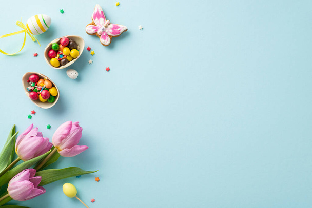 Exibição da doçura da primavera: Vista superior de pão de gengibre divertido, ovos de chocolate, doces e polvilhas de açúcar em um fundo azul claro com espaço para sua mensagem - Foto, Imagem