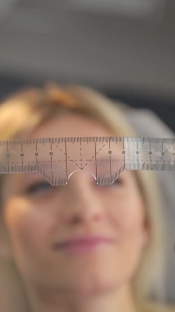 A young woman makes an eyebrow correction procedure in a beauty salon. Ruler for eyebrow architecture. Spa beauty salon. Vertical video - Footage, Video