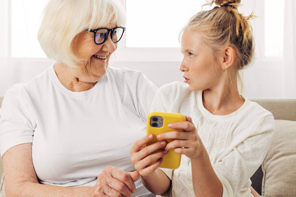 Совместимость видео-копия бабушка обнимая телефон образования связи семьи улыбаясь футболка в помещении диван ребенок называет пространство белой внучкой фотографии селфи - Фото, изображение