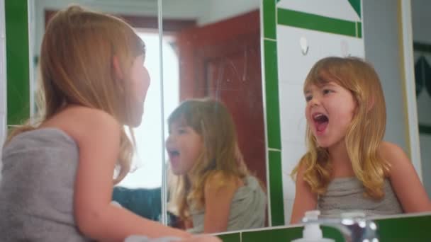 Roztomilá holčička sedí před zrcadlem v koupelně v ručníku se podívá na sebe a hraje si a směje se. - Záběry, video