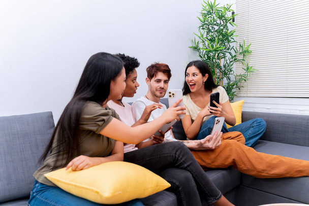 Amigos entusiasmados sentados no sofá compartilhando conteúdo de smartphones, envolvidos em interação digital.  - Foto, Imagem