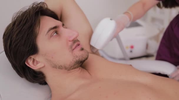A cosmetologist performs a laser hair removal procedure on the armpit of a handsome male patient in a beauty salon. Beauty and skin care concept. - Séquence, vidéo