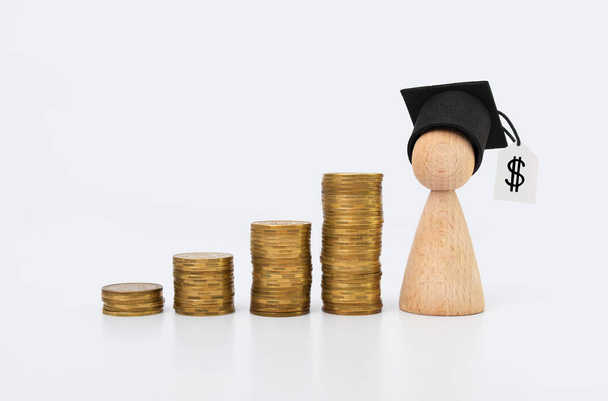 Concept d'éducation financière et de littératie. Homme en bois avec un chapeau de graduation et des pièces d'or sur un fond clair - Photo, image