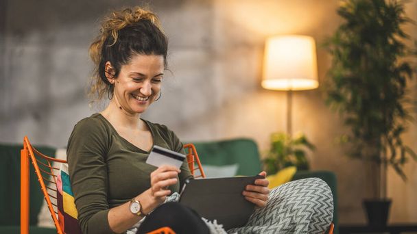 Одна жінка доросла біла жінка вдома щаслива посмішка тримає банківську кредитну картку і цифровий планшет онлайн покупки концепція електронного банкінгу реальні люди копіюють простір електронної комерції зробити покупку або бронювання - Фото, зображення