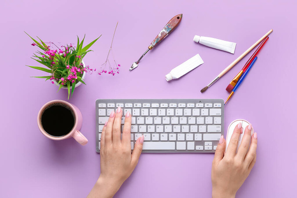 Kobiece ręce z nowoczesną klawiaturą komputerową. mysz, filiżanka kawy i artykuły malarskie na fioletowym tle - Zdjęcie, obraz