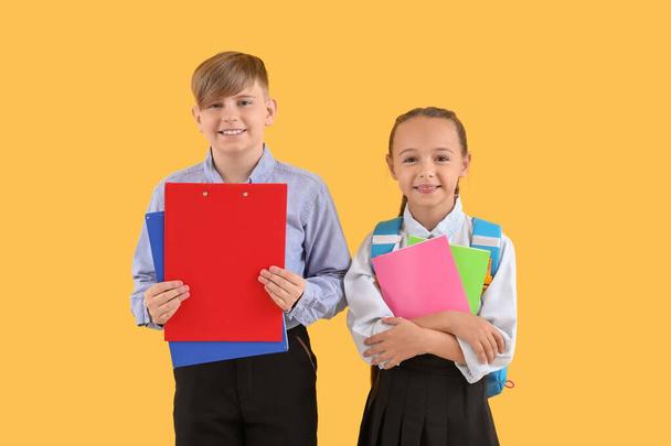 Μικρά συμμαθητές με στυλάτη στολή με σημειωματάρια σε κίτρινο φόντο - Φωτογραφία, εικόνα