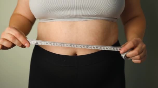 Close up footage of tape measure for measuring body. Unrecognizible girl or woman unwinds tape measure and is ready to measure her waist. concept of weight loss, healthy lifestyle, doing home sports - Footage, Video