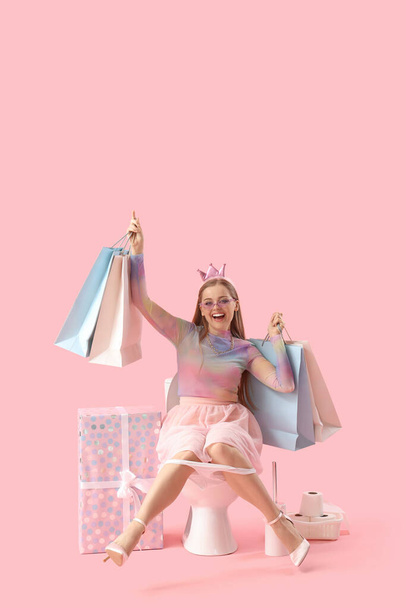 fiatal nő bevásárló táskák ül WC-n tál rózsaszín háttér - Fotó, kép