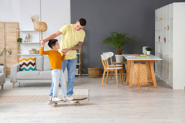 Młody człowiek ze swoim synkiem jeździ w domu na łyżwach - Zdjęcie, obraz