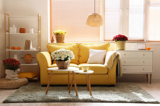 Interieur eines stilvollen Wohnzimmers mit gelbem Sofa und Chrysanthemenblumen auf Couchtisch - Foto, Bild