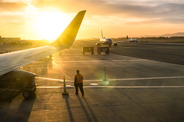 Pracy mężczyznę idącego w pobliżu skrzydło samolotu przy bramie terminala międzynarodowego portu lotniczego podczas zachodu słońca - pojęcie emocjonalną podróż dookoła świata - Soft focus i słońce Flara obiektywu z podświetleniem - Zdjęcie, obraz