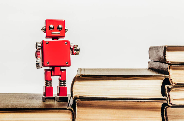 白い背景に赤いロボットのおもちゃが立っている古いアンティークブックスタックの写真. - 写真・画像