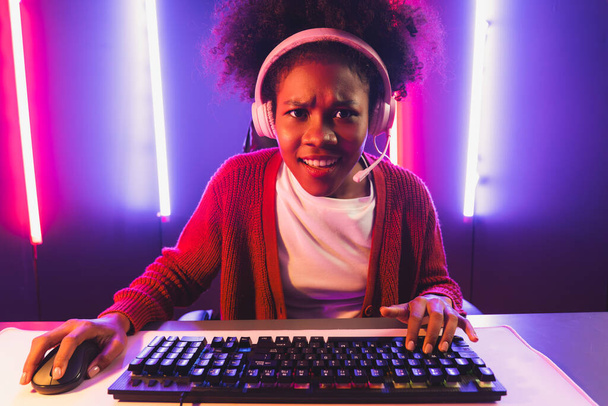Streamer gier, afrykańska dziewczyna gra online walki z Esport wykwalifikowany zespół noszenia słuchawek w neonowym kolorze oświetlenie pokoju. Rozmawianie z innymi graczami struganie strategii, aby wygrać konkurentów. Tastemaker. - Zdjęcie, obraz