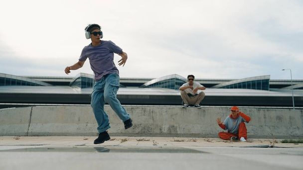 Bir grup yetenekli break dansçı, ona bakan ve tezahürat yapan arkadaşlarıyla sokak dansı yapıyor. Yakışıklı hippi çocuk sokakta müzik dinlerken dans ediyor. Açık hava sporu 2024. Yumuşak bir şekilde.. - Fotoğraf, Görsel