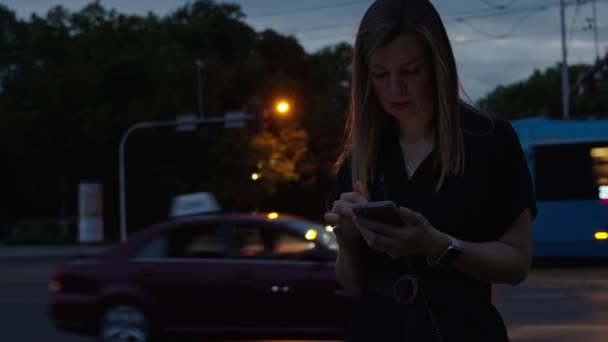 Vrouw gebruikt smartphone op nachtstraat, het lezen van sociale media en surfen op internet. De persoon houdt de telefoon in de hand, drukt met bewegende auto 's tegen de nachtstraat. Online verslaving - Video