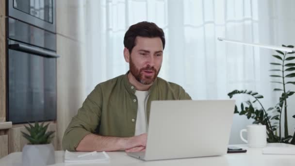 Kaukázusi szakállas férfi alkalmi ruhában modern laptoppal és internet kapcsolattal az online interjúhoz. Jóképű fickó megbeszéli a munka részleteit a munkaügyi céggel a munkahelyen.. - Felvétel, videó