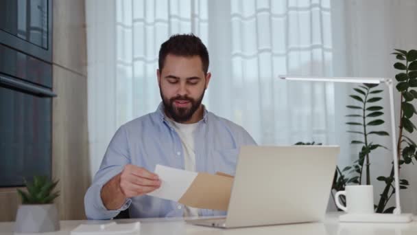 Shocked bearded man opening envelope and staring at letter while saying what and leaning head on hand at home. Caucasian person getting surprisingly huge bills from hospital for medical testings. - Footage, Video